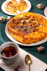 Traditional homemade banana caramel pie. French Tarte Tatin on a white plate with a cup of tea on a green, emerald background. Top view. Close-up.
