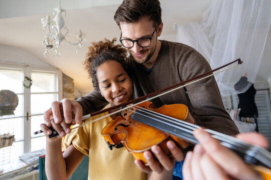 Private music man teacher giving violin lessons to African American girl at home