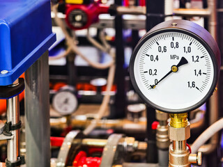 Pressure gauge displaying measurement in an industrial setting with various pipes and valves at a manufacturing facility