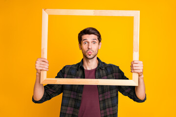Photo of funny guy holding wooden picture frame looking through it sending air kiss wear casual...
