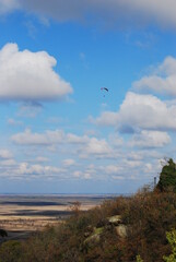 Paraglider in the blue cloudy sky with fields in the background