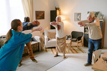 Wide shot of biracial senior residents of nursing home standing in circle while stretching back...