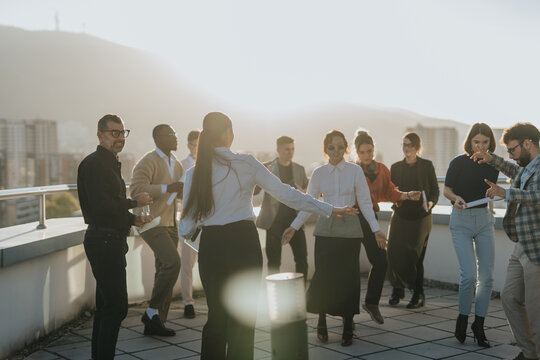 A group of business colleagues enjoy a lively celebration with dance and music on a high-rise balcony at sunset, showcasing a festive and energetic atmosphere.