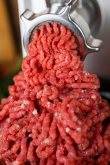 The concept of healthy and proper nutrition, cooking. A close-up view from above of red ground beef with streaks of fat, which comes out of the metal grinder in waves and takes up most of the photo