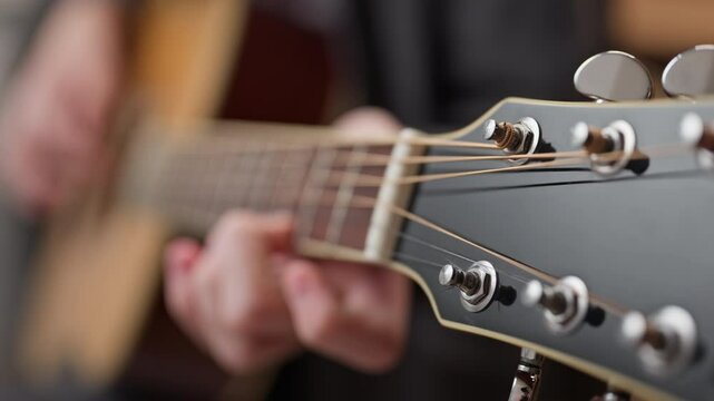 Selective focus on guitar tuning pegs and strings in out of focus bokeh young man playing guitar.
