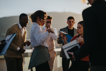 A group of multicultural business people celebrate on a high-rise balcony. They enjoy the sunset,...
