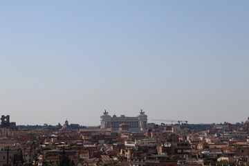 Panoramic view of Rome with the Altare della Patria monument in the center, surrounded by historic buildings under a clear blue sky.