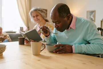 Medium close up of senior resident of African American man with disability eating chicken soup while having lunch time
