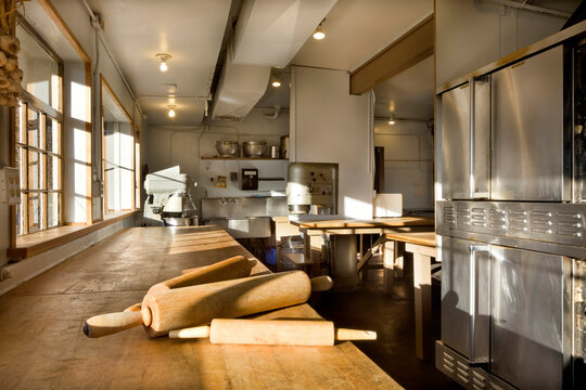 A commercial bakery with row of ovens and preparation area, a wooden board with three rolling pins.