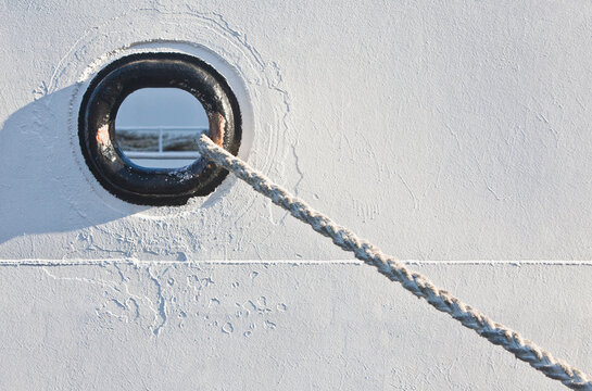 A hawser hole and hawser or mooring rope of a docked boat in a harbour.