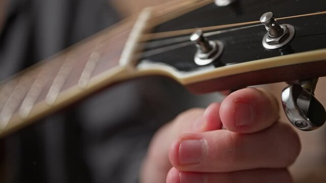 Tuning a new guitar. The musician uses a peg on the fretboard to tighten the string to get the right sound.