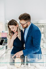 Beautiful couple enjoying in shopping at modern jewelry store. Young woman try it out gorgeous and...
