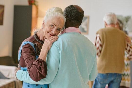 Portrait of elegant senior woman looking at camera while her unrecognizable partner hugging her during dance