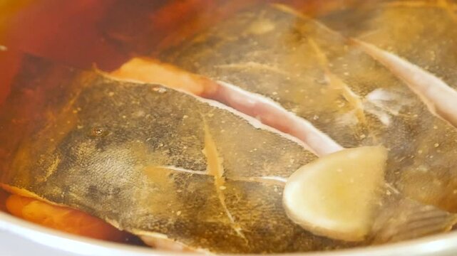 和食の魚の煮付け。新鮮なナメタカレイに調味料をかける動画。クローズアップ。左から右へ。