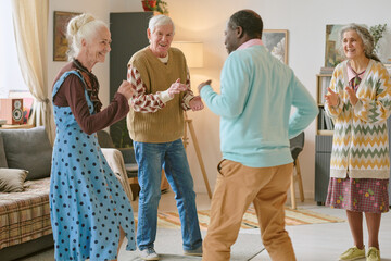 Wide shot of multiracial senior people dancing in center of living room in nursing home, they keeping rhythm and enjoying spare time