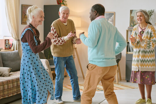 Wide shot of multiracial senior people dancing in center of living room in nursing home, they keeping rhythm and enjoying spare time