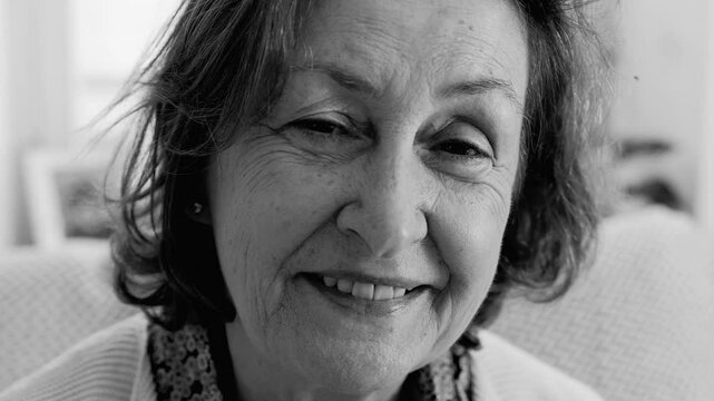 Senior woman smiling, close-up portrait in black and white, natural expression, wrinkles, warmth, elderly lady, happy face, wisdom in eyes, comfortable home setting, intimate moment