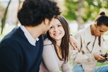 Obraz premium A joyful moment among young friends in a park, with one person focused on their phone. The atmosphere is relaxed and cheerful, highlighting friendship and connection.