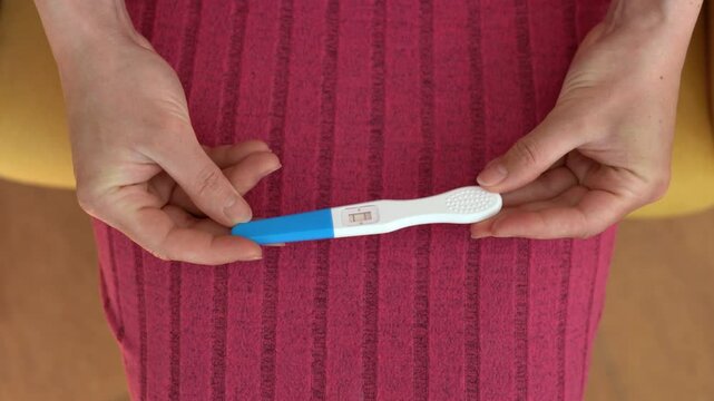 Close up woman's hands slowly turning positive pregnancy test, two lines clearly shown.