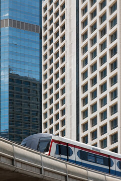 A mass transit train on an elevated track passing modern buildings in the central business district of Bangkok.