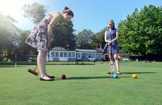 Two young women standing on a lawn, playing croquet.