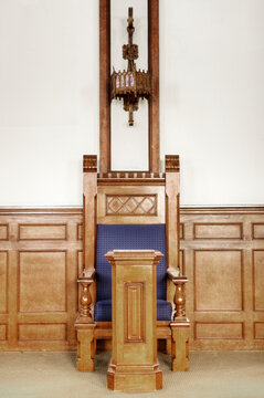 A ceremonial chair in a large auditorium in a historic building with a blue seat and podium.