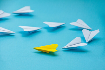 Close up view of yellow paper airplane origami leading white airplanes on blue background with...