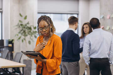 African american businesswoman holding a folder, diverse professionals collaborating during high tech meeting, discussing strategy while using digital devices in modern workplace environment