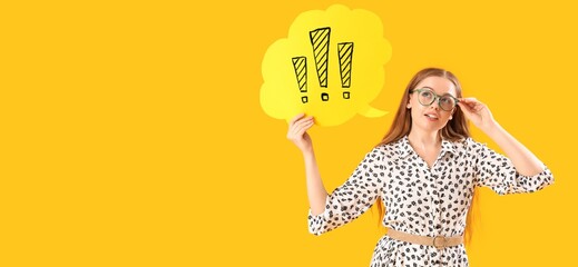 Young woman in eyeglasses holding speech bubble with exclamation marks on yellow background with...