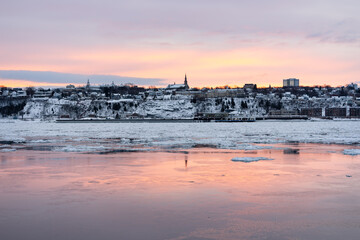 Church dominating the south shore cityscape over the partly frozen St. Lawrence river seen during a hazy winter sunrise, L&eacute;vis, Quebec, Canada