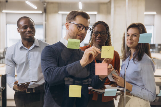 Group of diverse professionals brainstorming and collaborating on a project using sticky notes in a modern office setting