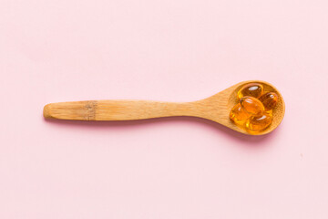 Vitamin omega capsules in a spoon on a colored background. Pills served as a healthy meal. Red soft gel vitamin supplement capsules on spoon