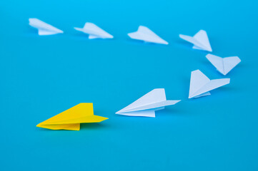 Side view of yellow paper airplane origami leading other white airplanes on blue background with customizable space for text. Business and Leadership skills concept