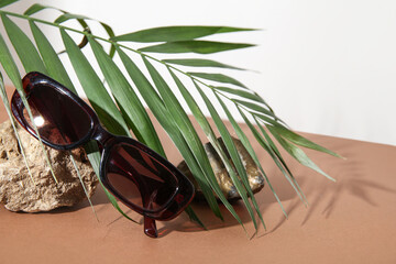 Stone with stylish sunglasses and palm leaf on brown table