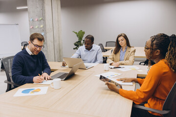 Professionals engaged in a business meeting, discussing charts and data on digital devices in a contemporary office environment