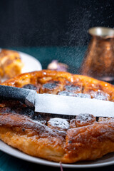 Put a knife on the pie and sprinkle powdered sugar on top to get the contour of the knife on the pie. On a dark background, powdered sugar falls on a banana tart