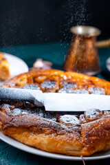 Put a knife on the pie and sprinkle powdered sugar on top to get the contour of the knife on the pie. On a dark background, powdered sugar falls on a banana tart
