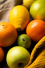 A bunch of fruit including apples, oranges, and lemons are on a table. The apples are green and the oranges are orange