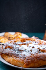 Banana Tarte Tatin is sprinkled with powdered sugar on a white plate on a dark background. The powder is poured onto the cake. Vertical Photo