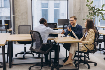Business professionals collaborating, exchanging ideas and handshaking during meeting in contemporary workspace with expansive glass windows