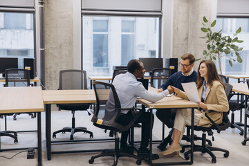 Three professionals engaged in a collaborative discussion in a contemporary office setting, emphasizing teamwork and diversity in business © anatoliycherkas