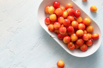 Bowl with sweet yellow cherries on light blue background