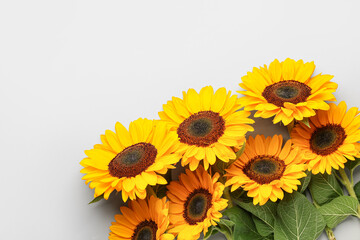Obraz premium Bright yellow sunflowers with green leaves on a light gray background, floral arrangement for summer and nature concepts