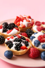 Plate of tasty tartlets with whipped cream and berries on pink background