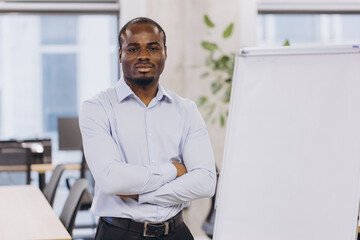 Fototapeta premium Professional african american businesswoman standing near blank flipchart, preparing for strategic presentation in sleek corporate workspace