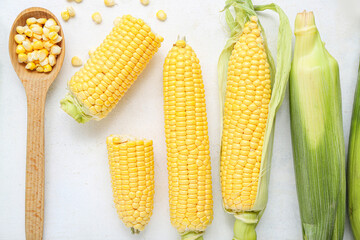 Fresh corn cobs and wooden spoon with kernels on white table