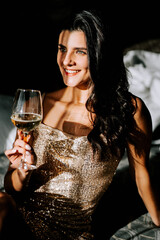Woman in a glittering dress enjoys a glass of wine in a cozy, softly lit space during an evening gathering