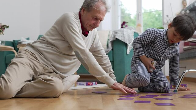 Grandfather and young boy playing memory game on floor, focused and engaged, cozy home setting, family bonding time, intergenerational connection, educational and fun activity, casual