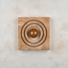 A wooden puzzle featuring concentric circles with a central sphere, showcasing a minimalist design and smooth surfaces.