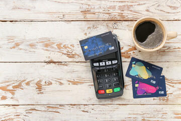 Payment terminal with credit cards and coffee cup on white wooden background